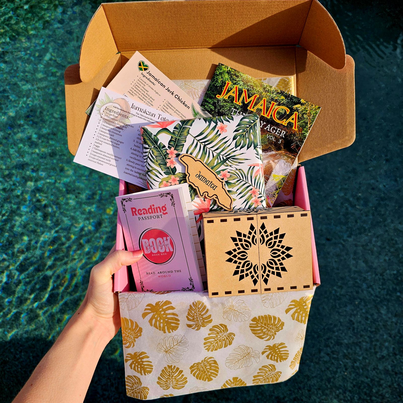 Open Jamaica book box with a wrapped book, travel guide, recipes, passport sticker, and a wooden sun box.