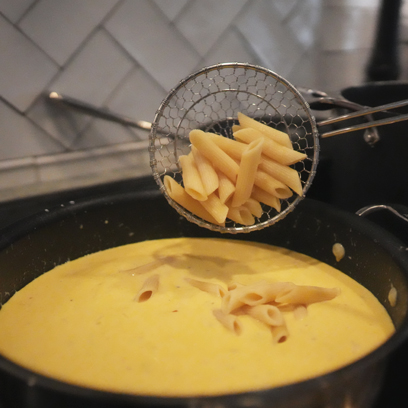 Adding penne to the sauce pan.