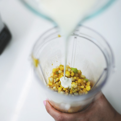Adding cream into blender with corn kernels.