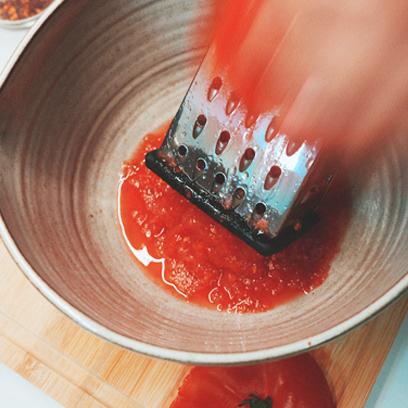 Grating tomato on the side of a box grater.