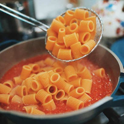 Tossing rigatoni into the sauce pan.