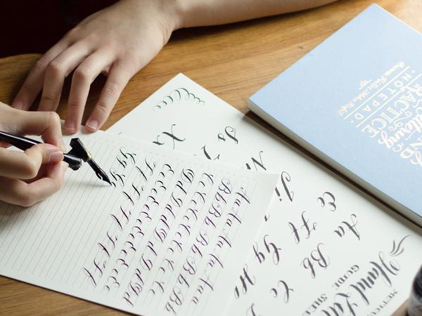 A person is sat at a table practising the calligraphy alphabet