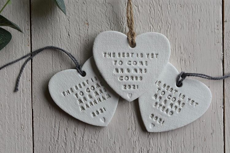 Three clay hanging heart ornaments sitting on a white-washed wood table