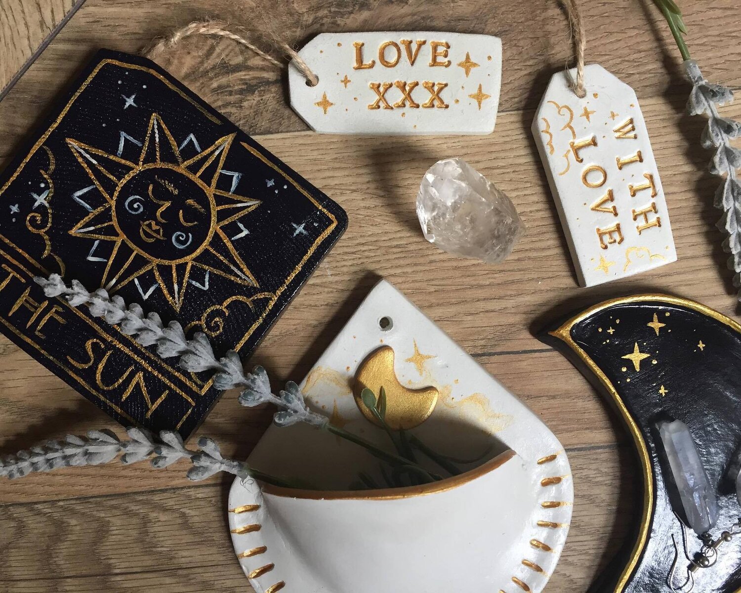 A white and gold moon-themed wall plant hanger sits in the middle of two black and gold tarot-themed clay hanging ornaments