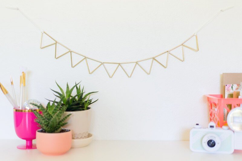 A triangular garland made from brass triangles hangs on the wall. Succulents and stationary lay decoratively on the table below.