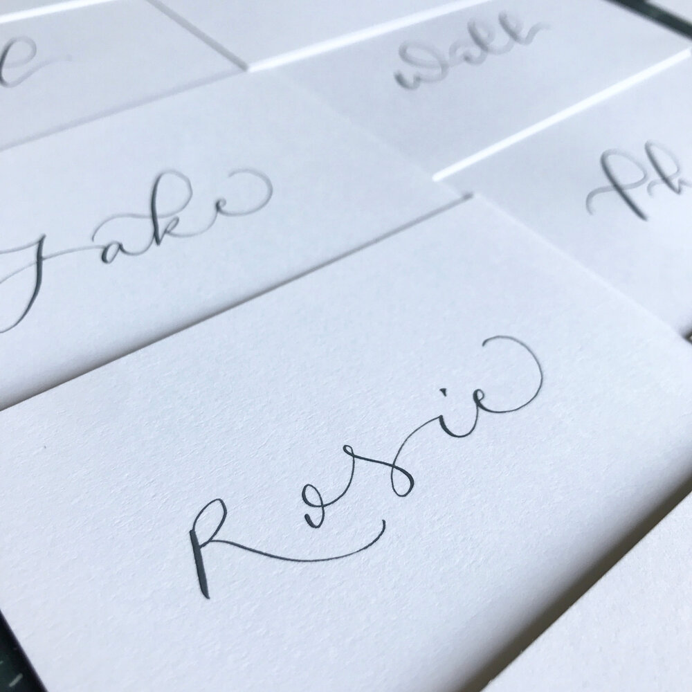 A collection of plain, white cards with calligraphy names on them