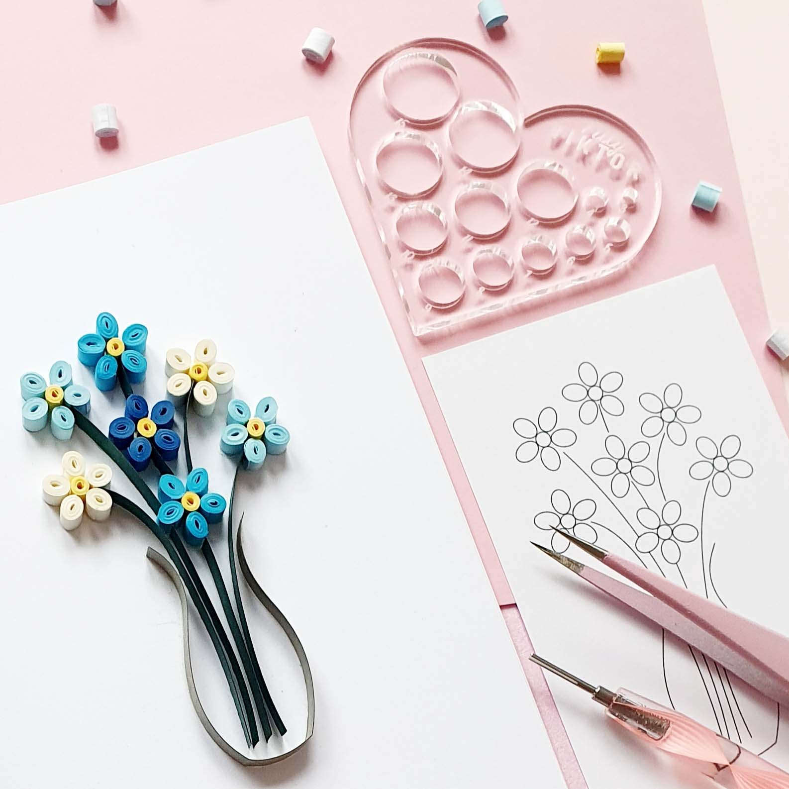 Flatlay photo of a quilled card with a flower on, surrounded by quilling tools and supplies