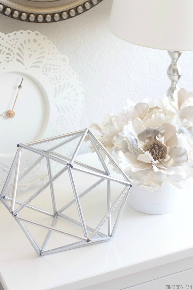 A silver-coloured geometric ball sits atop a white desk. A small bunch of white flowers are styled next to it.