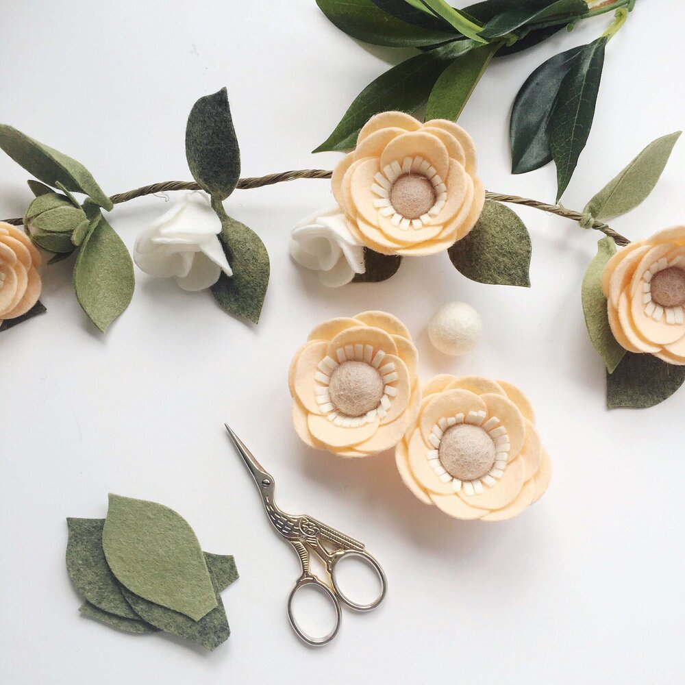 Image with a handful of small, peach-coloured felt flowers scattered amongst a green felt leaf garland.