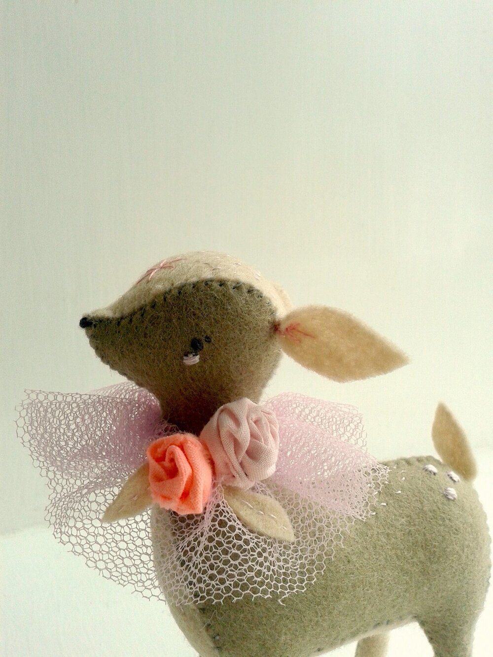 Image of a small, felted deer that is wearing a tiny rose necklace.