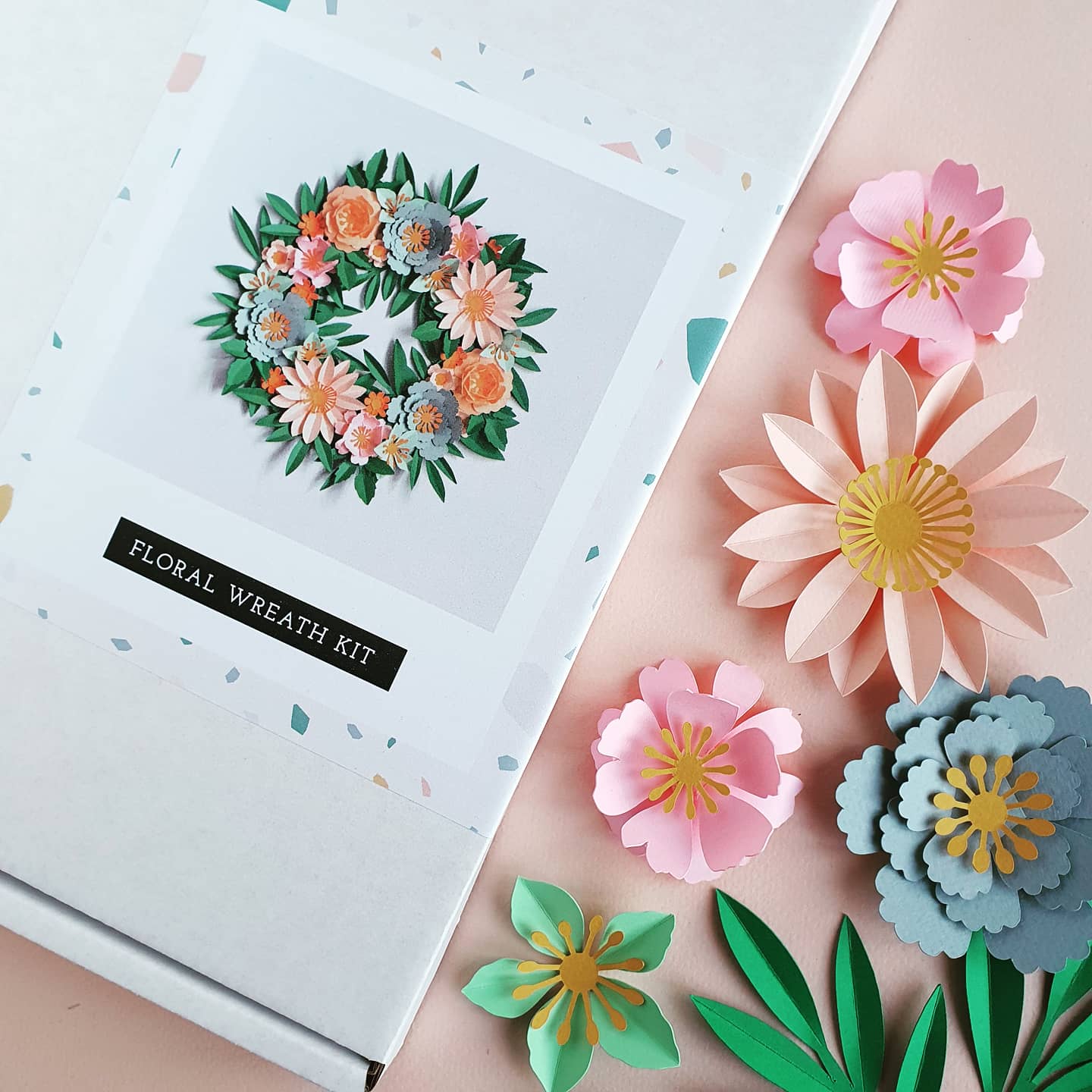 Papercraft wreath kit with pastel paper flowers next to the box