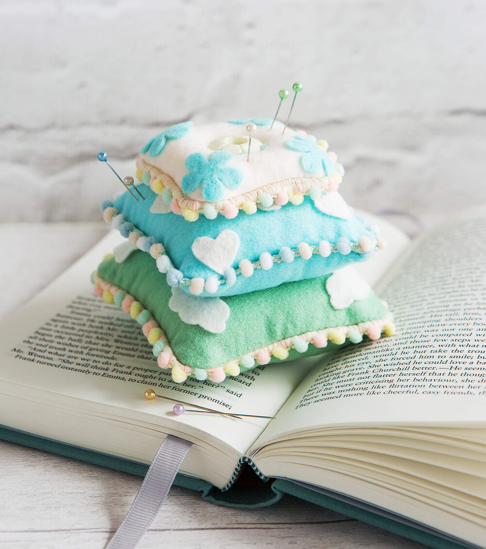 3 tiny felt cushion sit stacked upon an open book