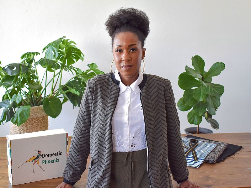 Woman standing in front of wood table with green bomber jacket, white shirt, and hoop earrings