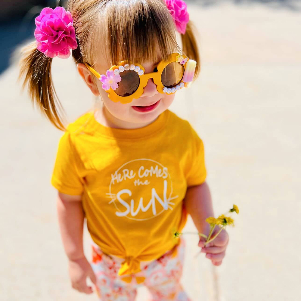 subscription box for girls unboxing toddler girl wearing a yellow Here Comes The Sun t-shirt from her Howdy Baby subscription box for little girls