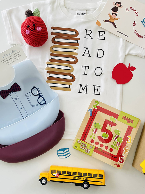 August 2023 Howdy Baby boxes for new moms with a happy apple toy, read to me onesie, and school bus pull back toy