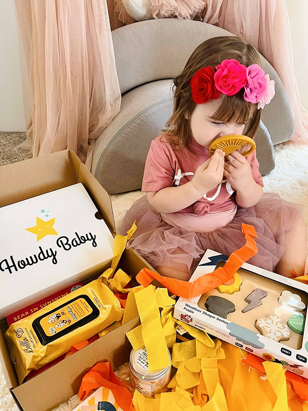 toddler girl unboxing a baby teether from her monthly Howdy Baby subscription box