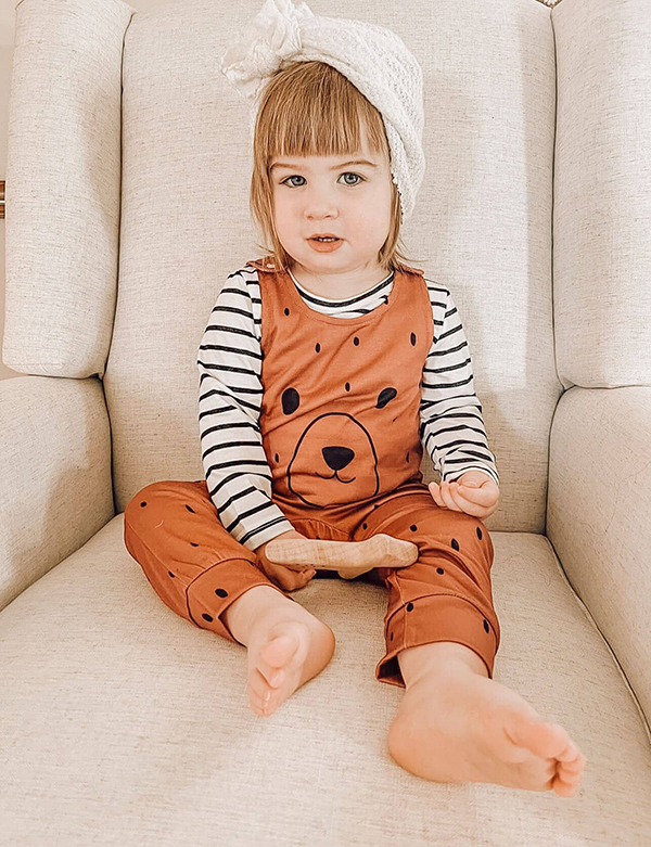 little girl wearing brown baby overalls holding a wooden teether