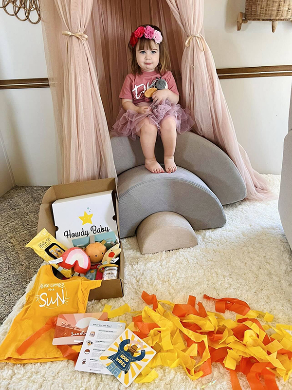 toddler girl holding her buzzbee stuffed animal while unboxing the April 2023 Howdy Baby Box