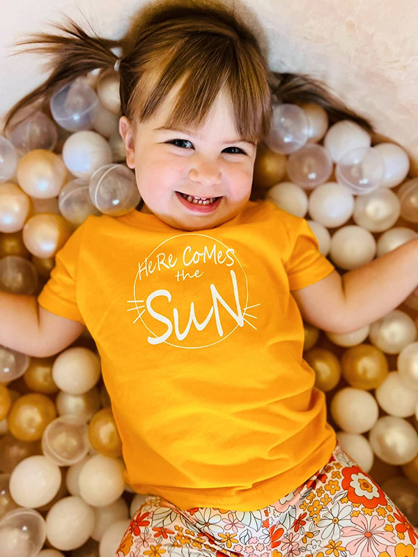 little girl wearing a bright yellow here comes the sun t-shirt