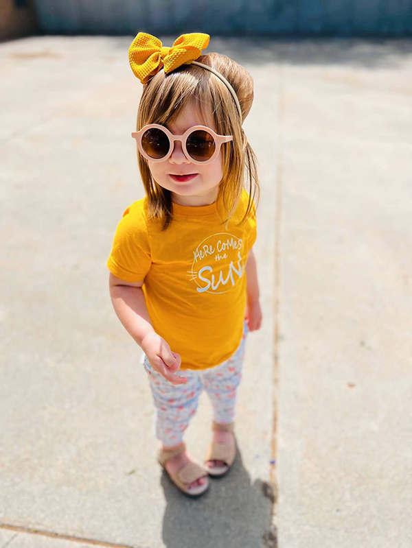 little girl wearing a yellow sunshine themed t-shirt from the April 2023 Howdy Kids Box