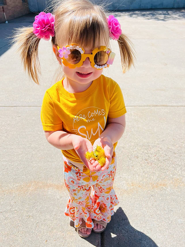 little girl wearing a sun themed onesie from the April 2023 Howdy Baby maternity box subscription