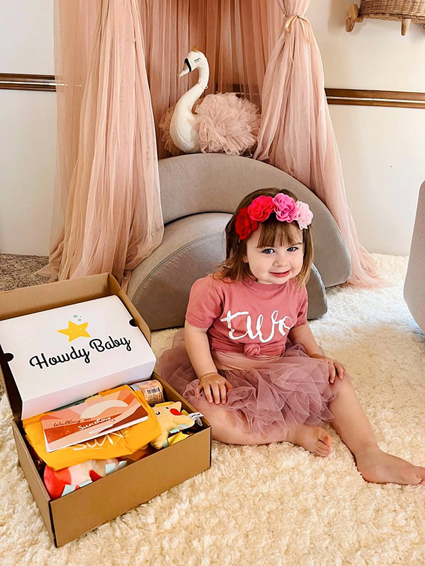 toddler girl sitting next to the Howdy Baby maternity subscription box