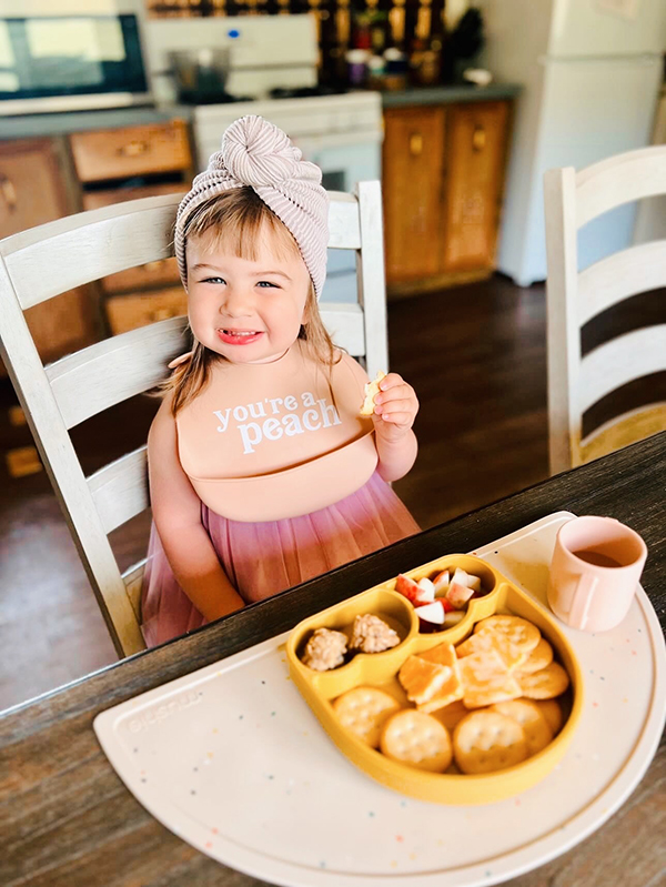 little girl eating food off of a rainbow shaped plate