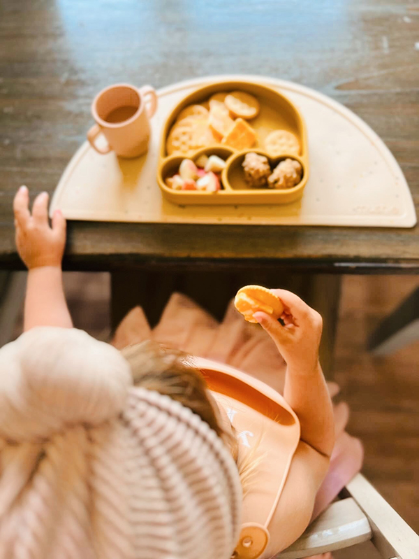 toddler eating food from a yellow silicone rainbow shaped plate