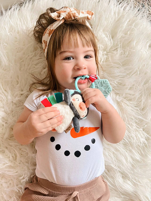 baby girl wearing a snowman onesie chewing on a winter sensory toy