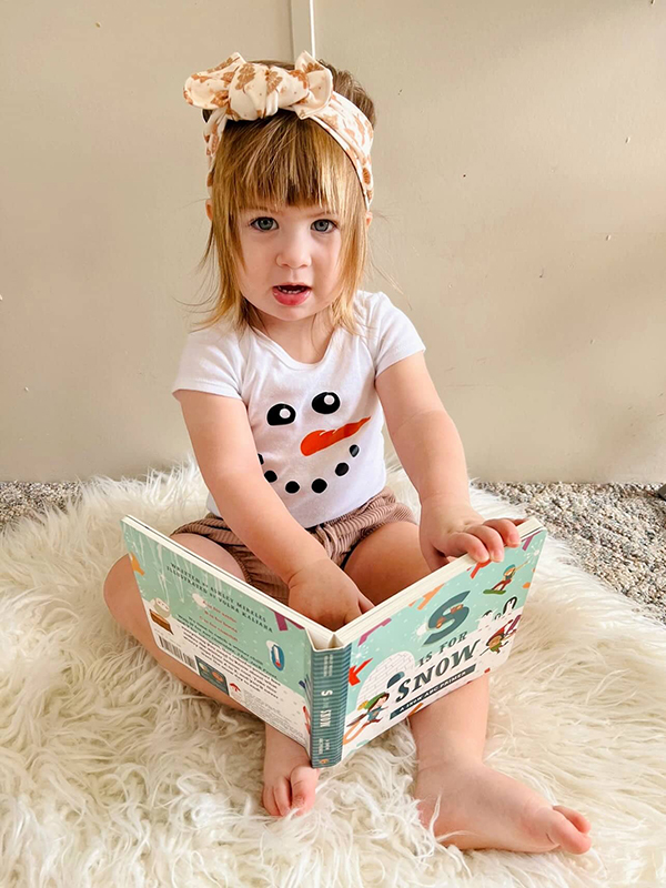 baby girl reading her monthly board book in a snowman onesie