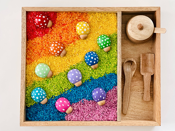 wooden ladybugs inside of a rainbow rice sensory bin