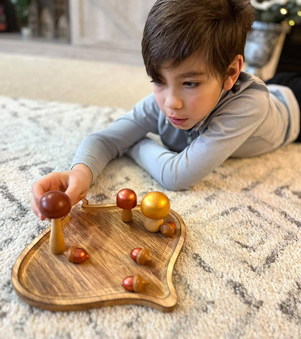 little boy playing with a wooden mushroom toy set