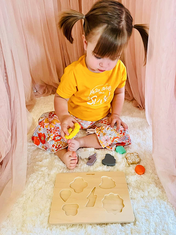 baby girl playing with a wooden weather themed Montessori puzzle