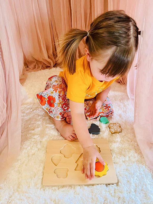 toddler girl playing with a wooden weather shapes puzzle