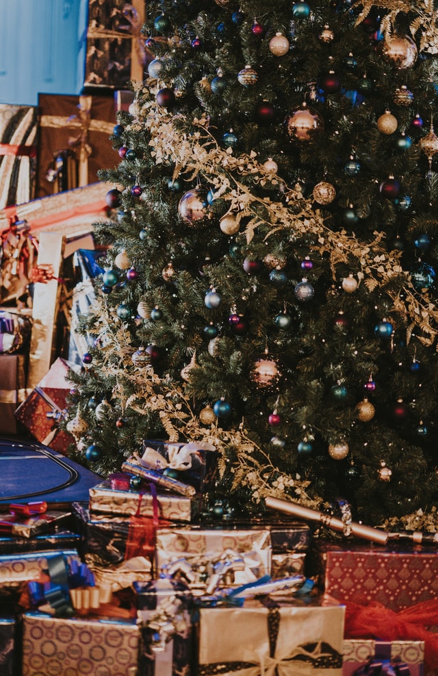 Christmas presents piled up under a lavishly decorated Christmas tree with twinkling lights. 