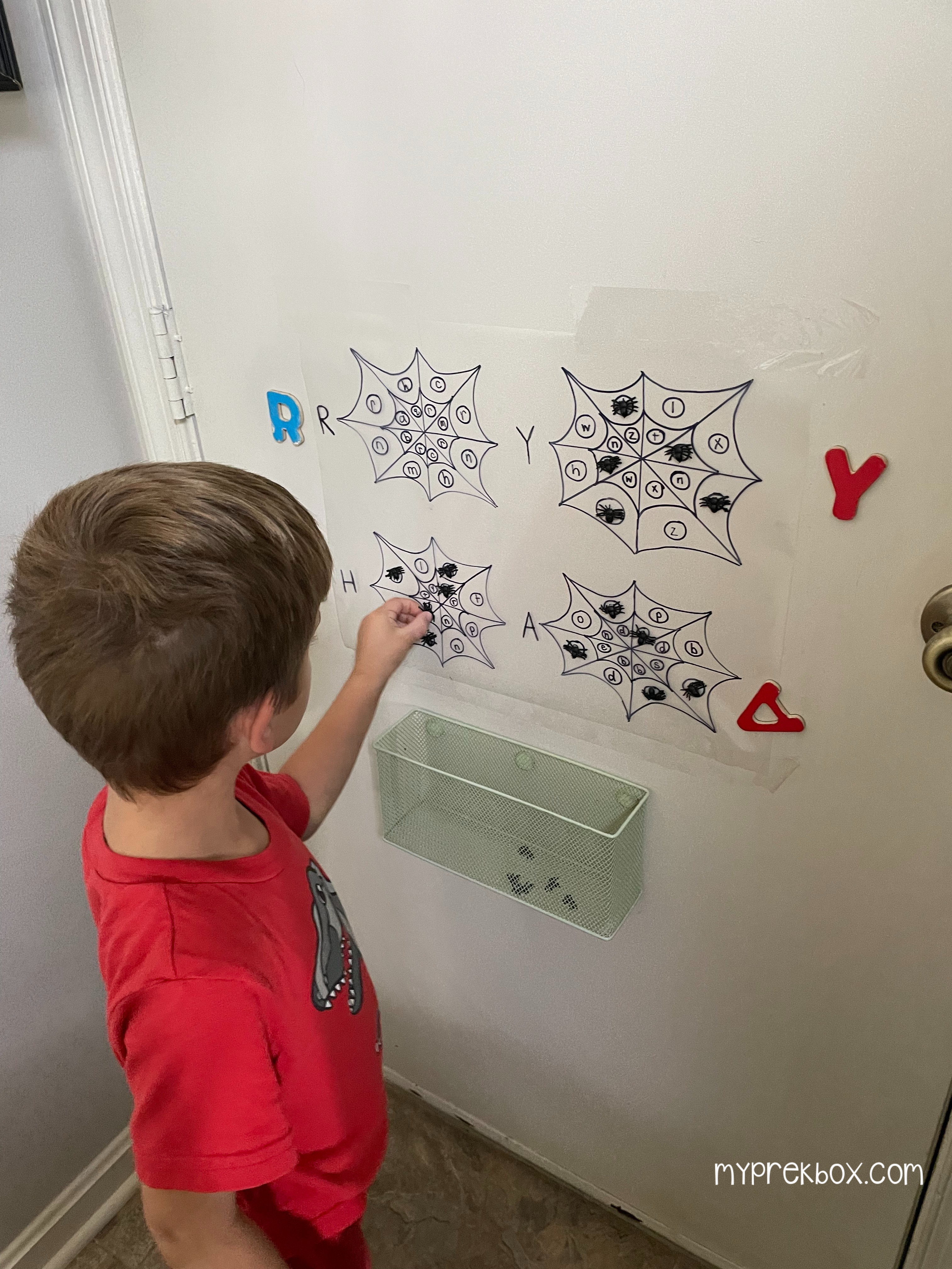 Preschool Halloween letter recognition Activity, kid standing next to wall with alpha web