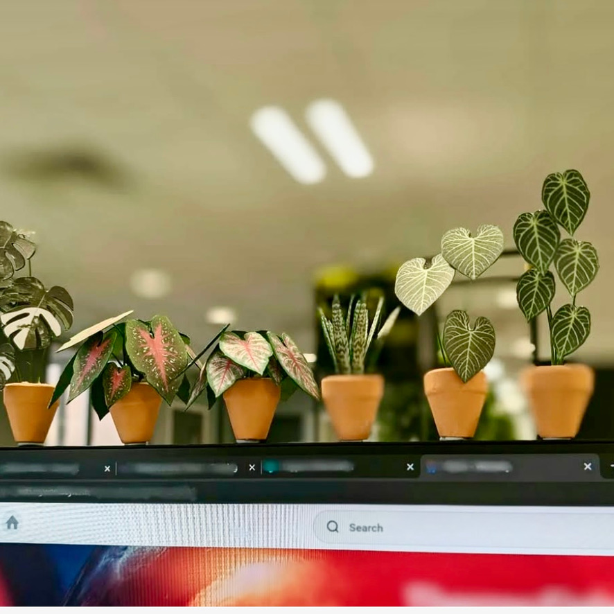 Mini paper plant lineup on office monitor Miniature handmade paper plants in terracotta pots lined up along the top of a computer monitor