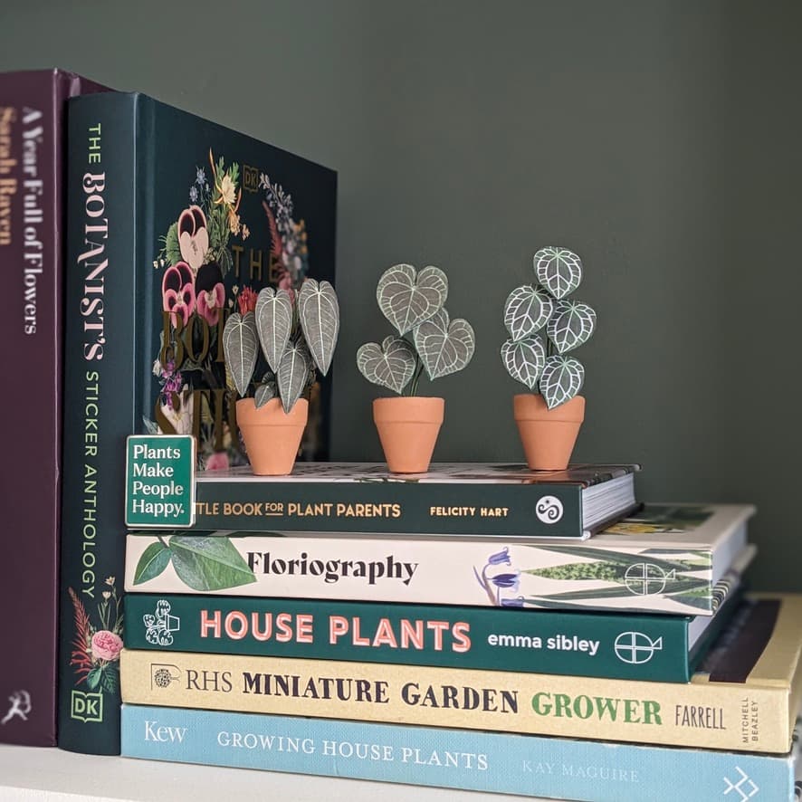 Mini paper plants styled on a plant book stack Miniature handmade paper plants in terracotta pots displayed on top of stacked houseplant books