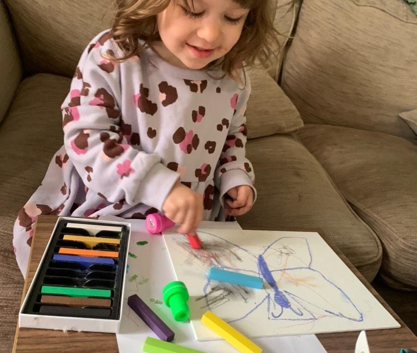 Little girl using soft pastels to colour in a drawing of a butterfly.