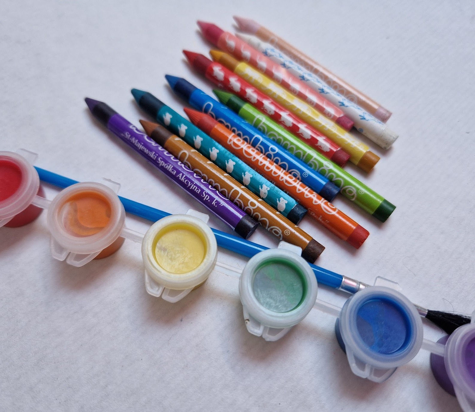 Rainbow coloured crayons and paints with a paint brush.