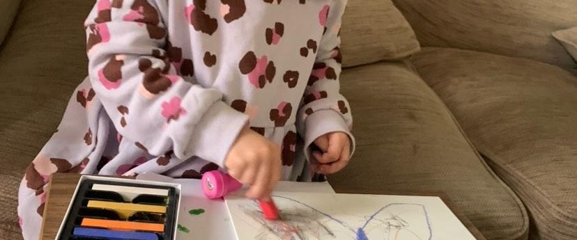 Little girl using soft pastels to colour in a drawing of a butterfly.