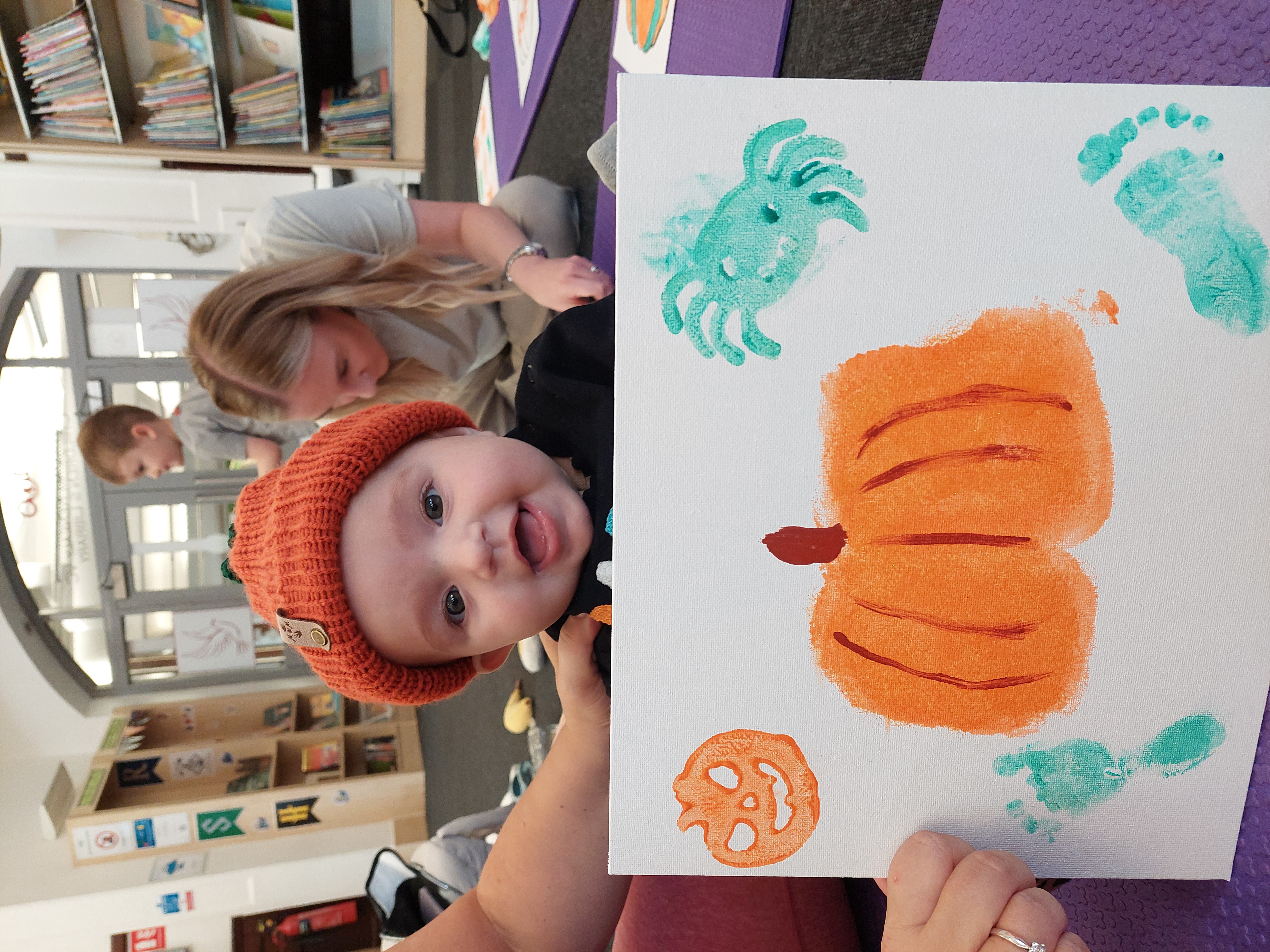baby posing with her Pumpkin painting that she made with her Mum in our halloween workshop