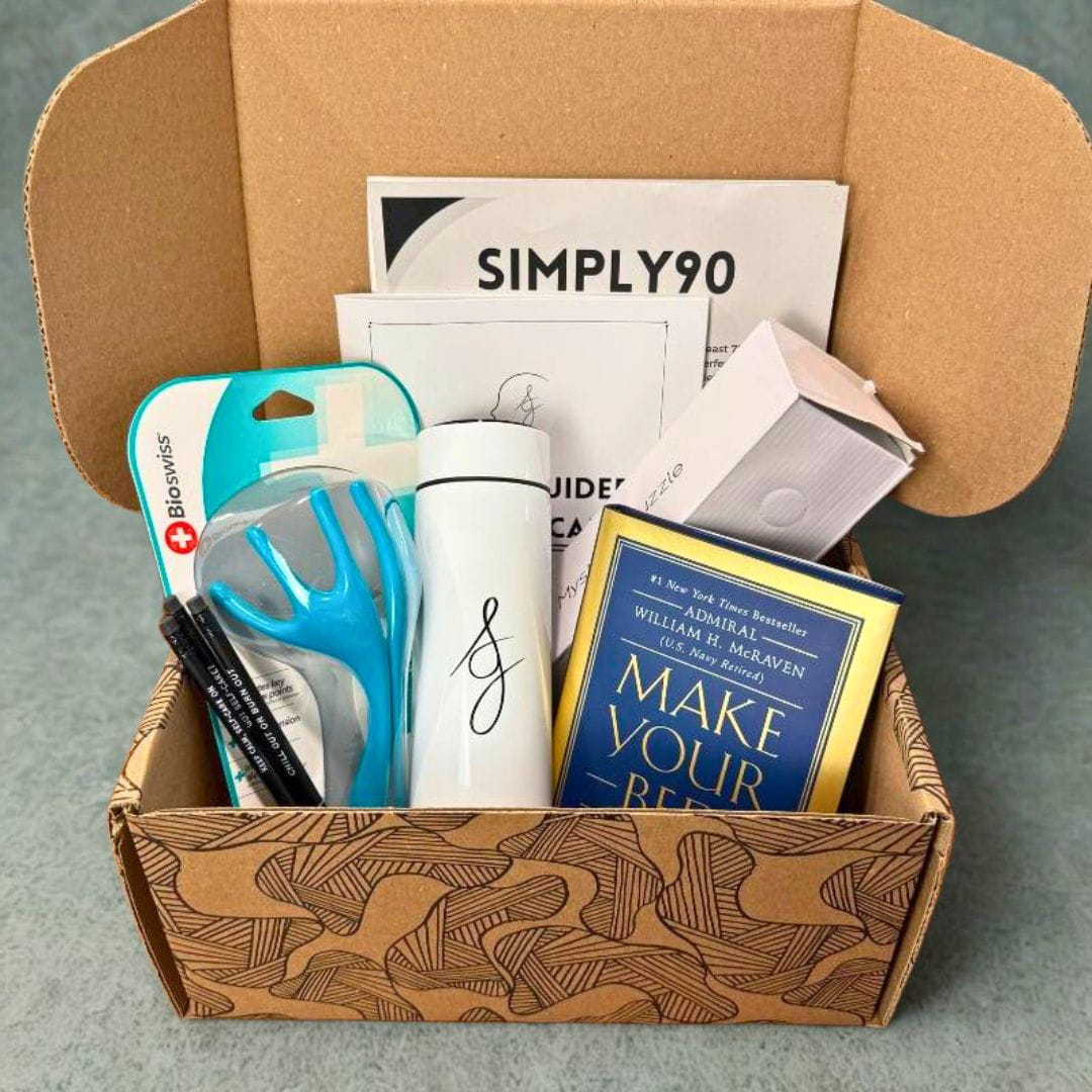 Open Simply Gray Burnout Box featuring wellness products like a water bottle, stress relief tools, a guidebook, and the book Make Your Bed.