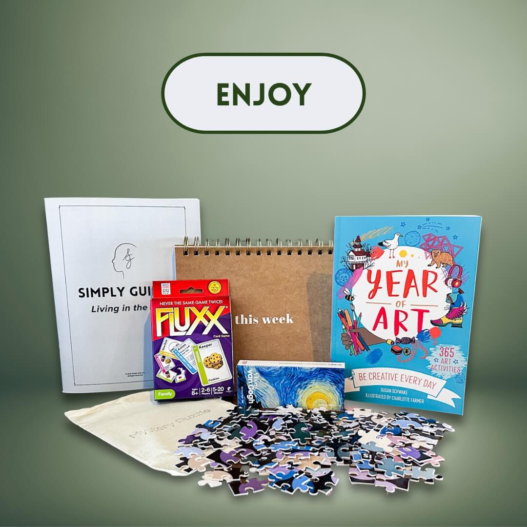 Simply Gray subscription box contents displayed with the word "ENJOY" above—featuring guidebook, puzzle, calendar, and games