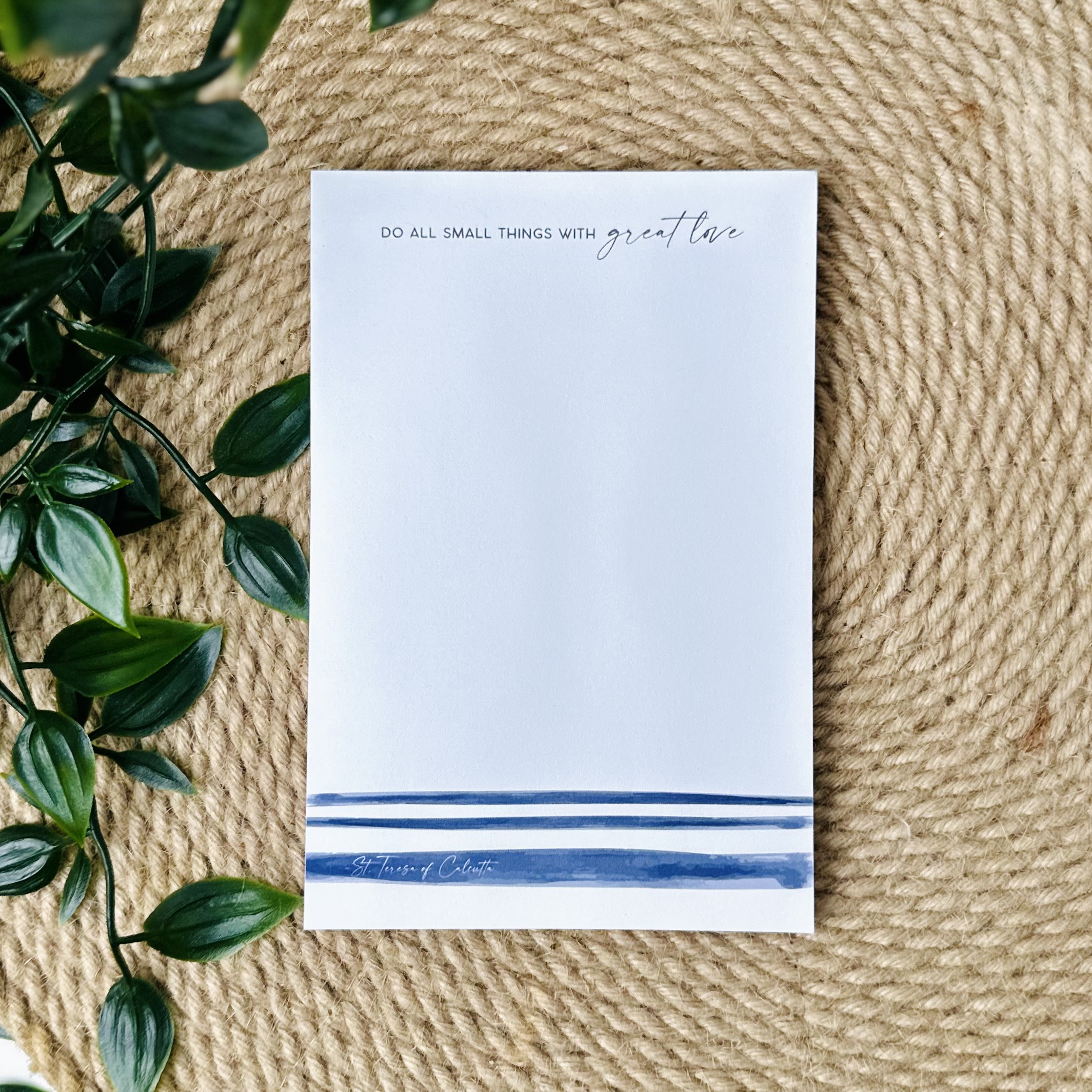 A notepad with blue watercolor stripes mimicking the stripes on the gown of Mother Teresa. The top of the notepad reads a quote Do all small things with great love.