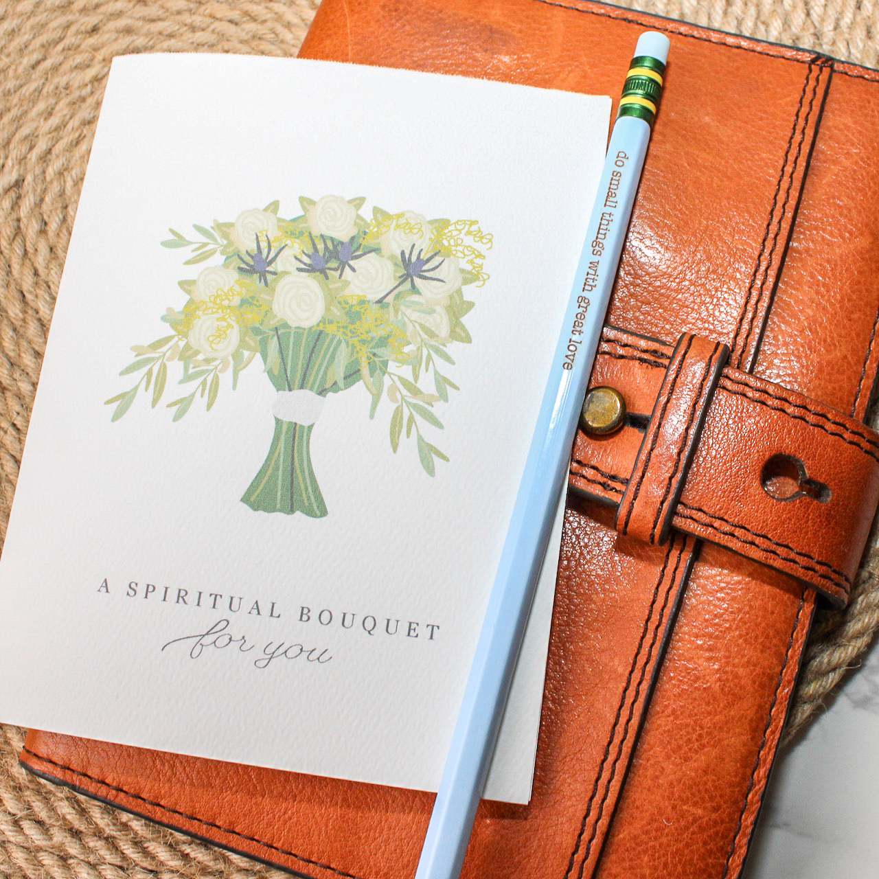 A spiritual bouquet greeting card sits on a notebook with a pencil that reads do small things with great love