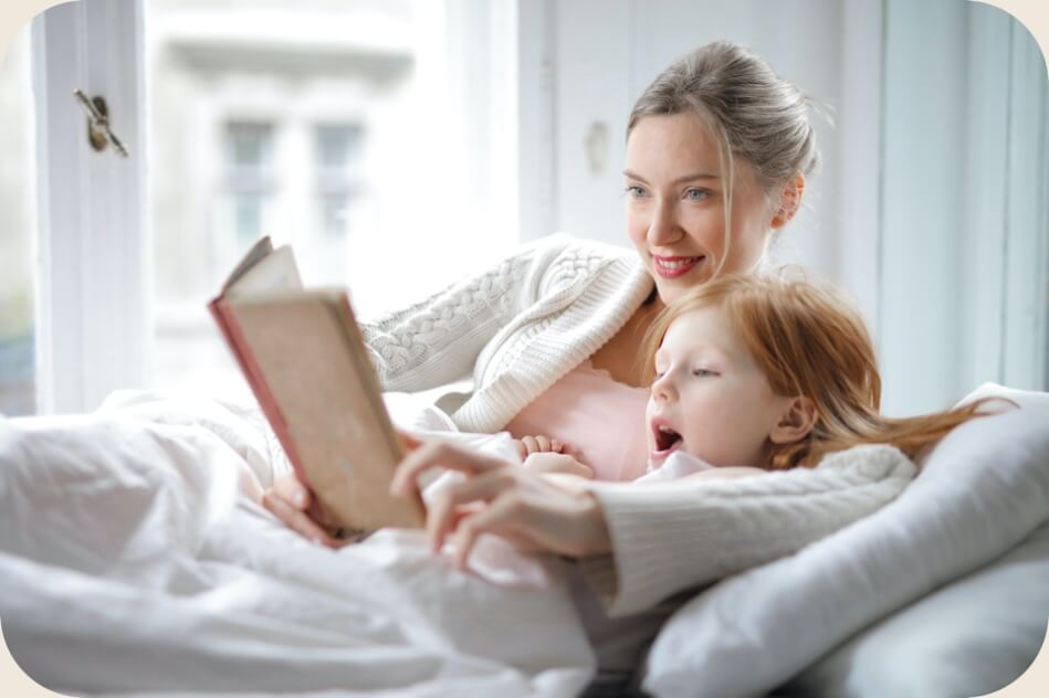 431-mom-and-daughter-reading-a-book-together-on-white-bed-16639489581783.jpg