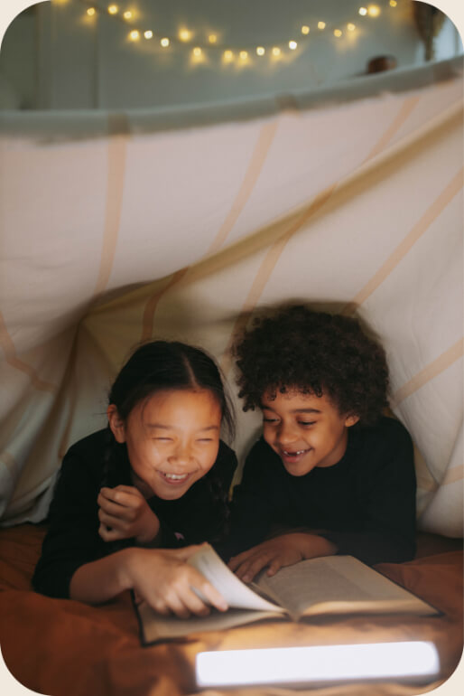 448-boy-and-girl-reading-and-laughing-under-a-blanket-fort-lit-by-string-lights-16639491292944.jpg