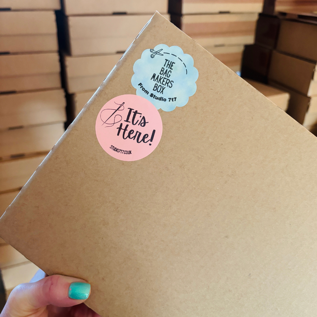 Cardboard box sealed with The Bag Maker’s Box and “It’s Here!” stickers from Studio 7t7.