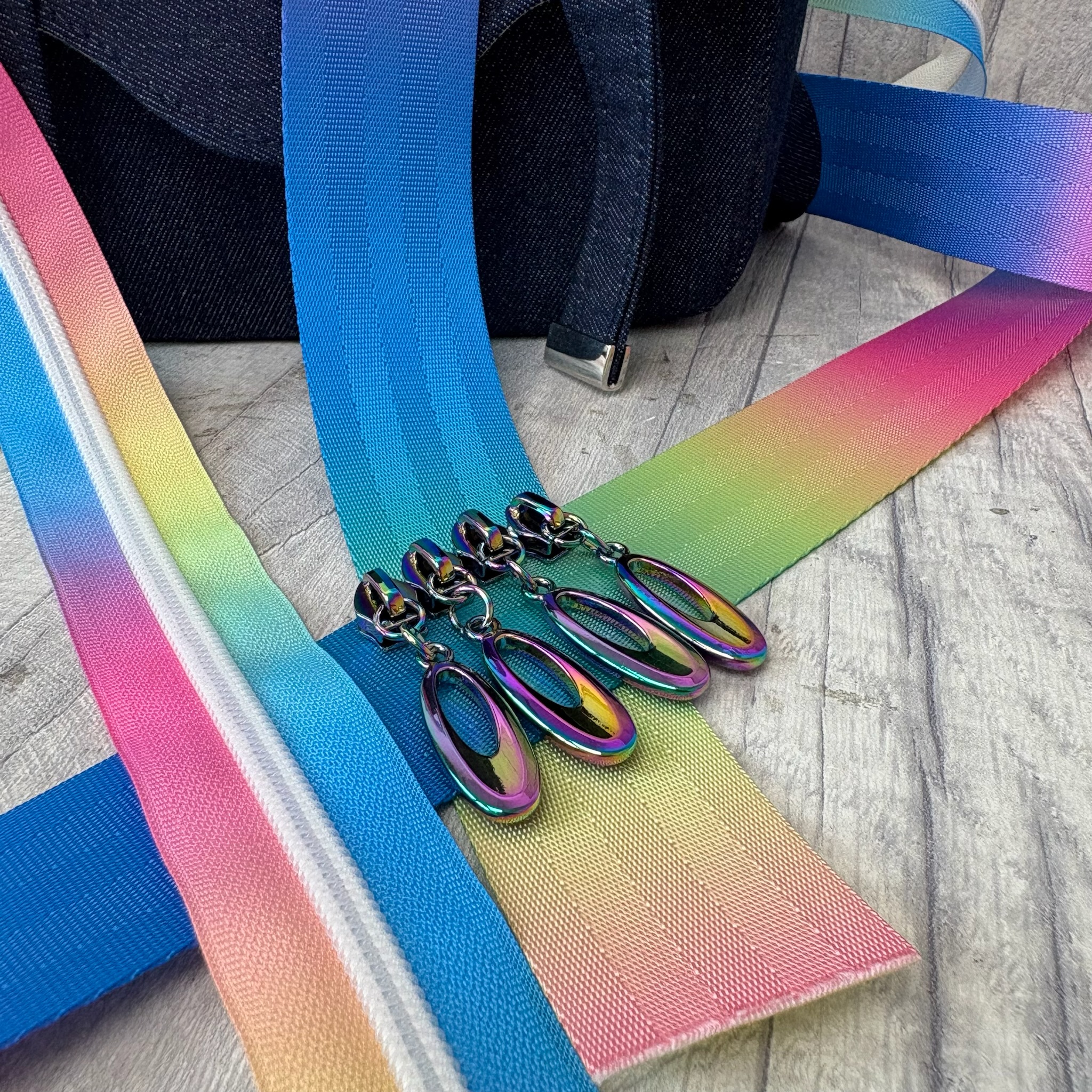 Colourful gradient zips and rainbow metallic bag hardware laid out on a wooden background.